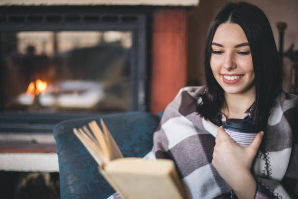 portrait de beau livre de lecture de femme par la cheminée - blanket fireplace winter women photos et images de collection