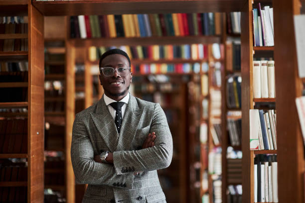 リーディングルームの図書館に立っているビジネススーツの中にある、ビジネススーツのアフリカの americanan アフリカ系アメリカ人男性 - bookshelf beautiful intelligence learning ストックフォトと画像