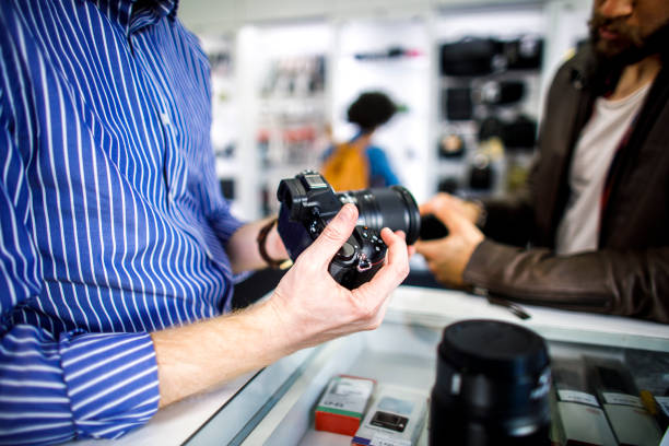 istock Shopkeeper holding a mirorrless camera while explaining it's functions to a customer in a camera store 1139037427