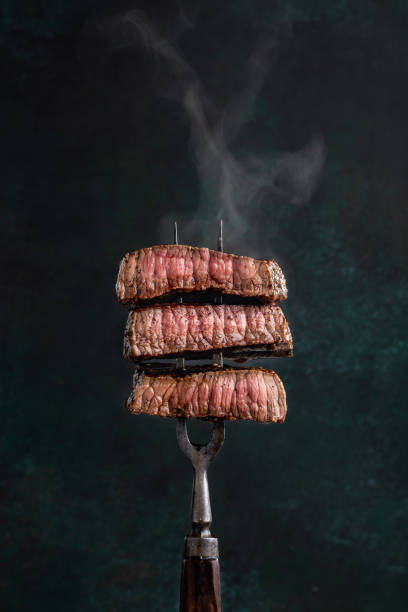 Beef slices on fork Slices of beef steak with steam on vintage fork on dark background steam photos stock pictures, royalty-free photos & images