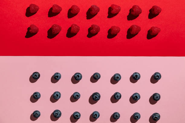 Two rows of raspberries on red background above three rows of blueberries on pink background