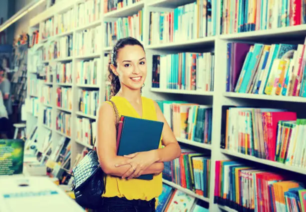 Young glad woman shopping books in hard cover in bookstore