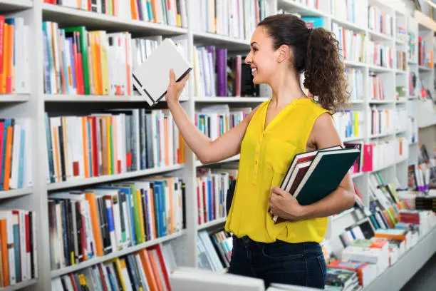 Young glad woman holding books in hard cover in bookstore
