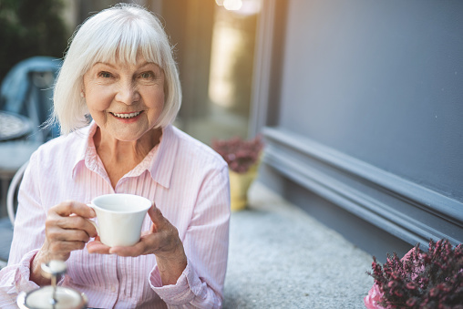 Joyful senior lady having hot drink outdoors