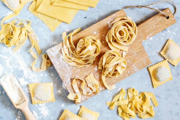 pasta italiana cruda de color amarillo, pappardelle, fettuccine o tagliatelle sobre un fondo azul, de cerca. huevo casero fideos proceso de cocción - pappardelle fotografías e imágenes de stock