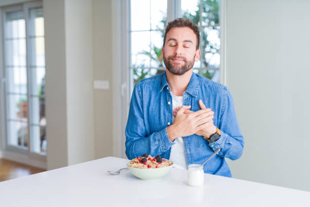 istock Handsome man eating cereals for breakfast at home smiling with hands on chest with closed eyes and grateful gesture on face. Health concept. 1139054507