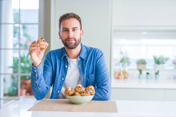istock Handsome man eating chocolate chips muffin with a confident expression on smart face thinking serious 1139054823