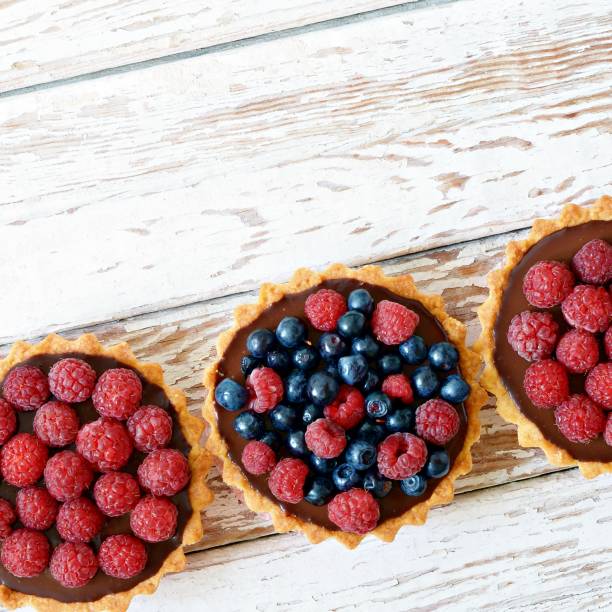 istock Raspberry and blueberry tartlets with chocolate ganache, fresh berries and mint leaves, selective focus. Fresh fruit tart on white background 1139056410