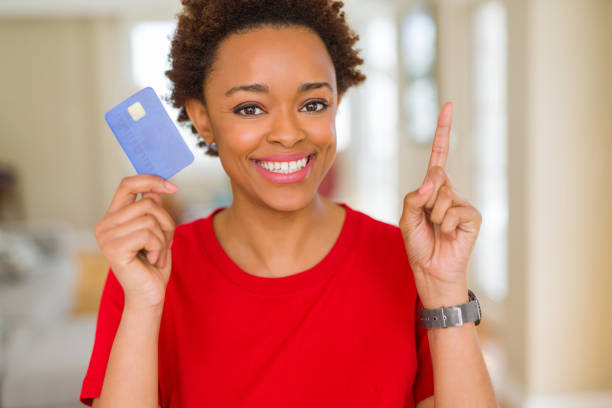 junge afrikanische amerikanische frau hält kreditkarte überrascht mit einer idee oder frage zeigen finger mit glücklichen gesicht, nummer eins - surprise ideas business person pointing stock-fotos und bilder