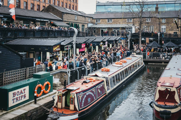 Tour boats moored on Regent's Canal inside Camden Market, London, UK, people walking around the market. London, UK - March 23, 2019:  Tour boats moored on Regent's Canal inside Camden Market, London, people walking around the market. In 2020 the Regentâs Canal will be 200 years old. camden market stock pictures, royalty-free photos & images