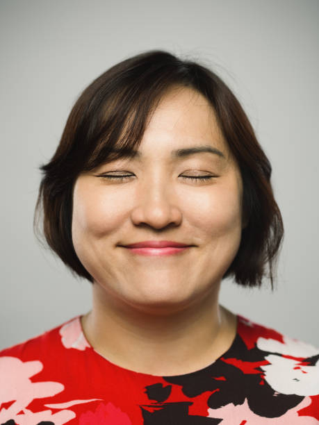 Portrait of real chinese mature woman with happy expression and eyes closed Close up portrait of asian mature woman with happy expression and eyes closed against gray white background. Vertical shot of chinese real people relaxed in studio with long brown hair. Photography from a DSLR camera. Sharp focus on eyes. older woman eyes closed stock pictures, royalty-free photos & images