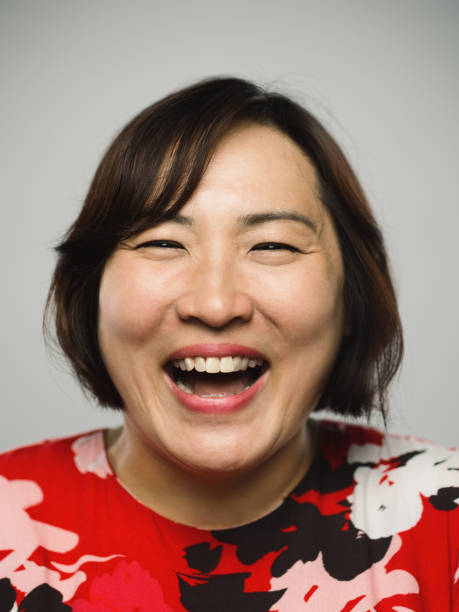 Portrait of real chinese mature woman with excited expression looking at camera Close up portrait of asian mature woman with excited expression looking at camera against gray white background. Vertical shot of chinese real people laughing in studio with long brown hair. Photography from a DSLR camera. Sharp focus on eyes. mouth open human face shouting screaming stock pictures, royalty-free photos & images