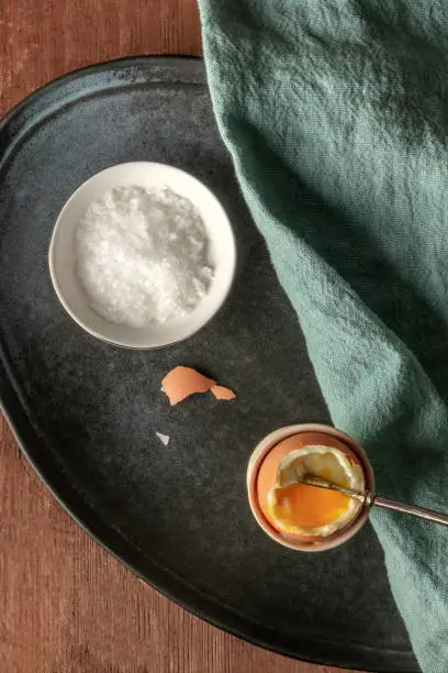 A soft-boiled egg in an eggcup with coarse sea salt and a spoon, shot from above