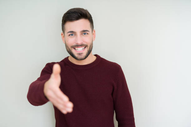 istock Young handsome man wearing a sweater over isolated background smiling friendly offering handshake as greeting and welcoming. Successful business. 1139065163