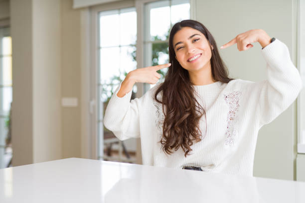 Young beautiful woman at home on white table smiling confident showing and pointing with fingers teeth and mouth. Health concept. Young beautiful woman at home on white table smiling confident showing and pointing with fingers teeth and mouth. Health concept. indian woman laughing stock pictures, royalty-free photos & images