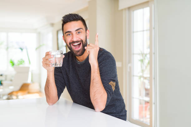 istock Handsome hispanic man drinking a fresh glass of water surprised with an idea or question pointing finger with happy face, number one 1139067189