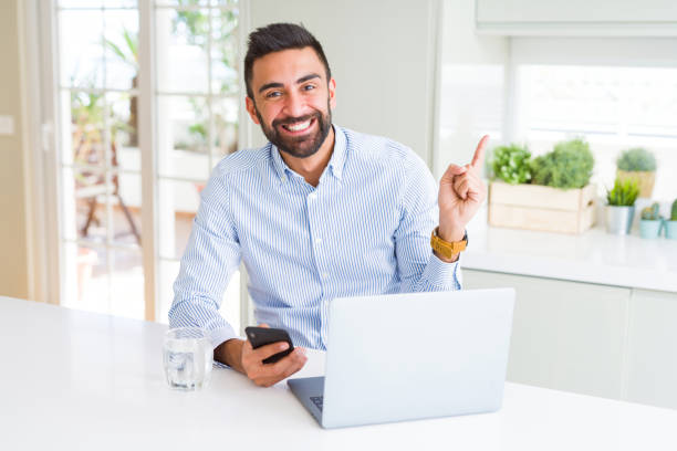 istock Handsome hispanic business man using laptop and smartphone very happy pointing with hand and finger to the side 1139067621