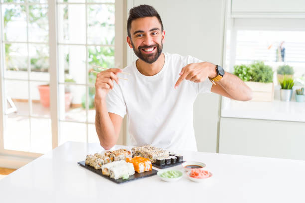 istock Handsome hispanic man eating asian sushi using chopsticks very happy pointing with hand and finger 1139068061