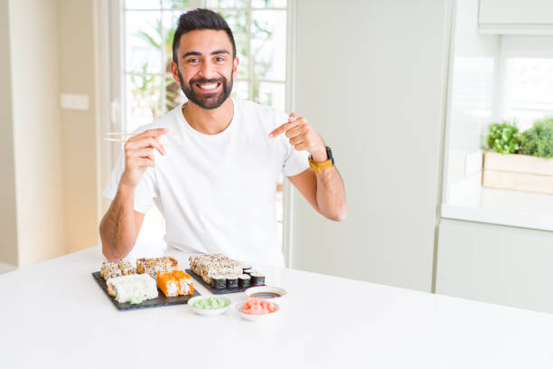 istock Handsome hispanic man eating asian sushi using chopsticks with surprise face pointing finger to himself 1139068623