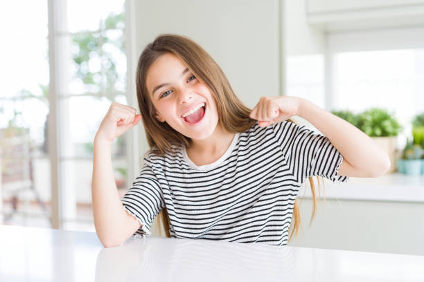 hermosa niña joven con rayas camiseta mostrando los músculos de los brazos sonriendo orgullosos. concepto de fitness. - clothing the human body long hair blond hair fotografías e imágenes de stock