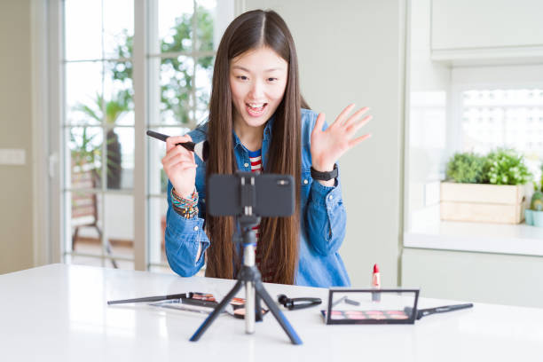 istock Beautiful Asian influencer woman recording make up tutorial using smartphone camera very happy and excited, winner expression celebrating victory screaming with big smile and raised hands 1139071201