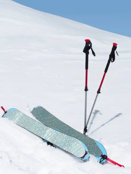 Splitboard halves with climbing skins and trekking poles at white snow background