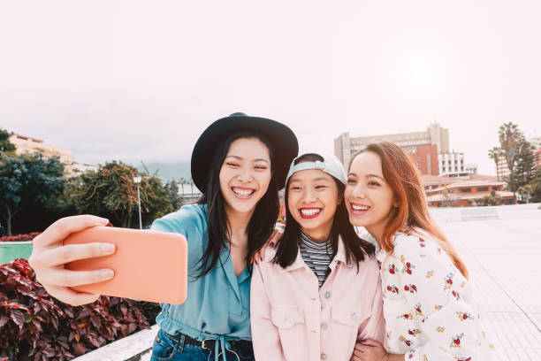 モバイルスマートフォン屋外で selfie を取る幸せなアジアの女の子-新しい技術アプリで楽しい若いトレンディなティーンエイジャー-人、社会、メディア、友情、ハイテクと若者のライフスタ - 日本　スペイン ストックフォトと画像