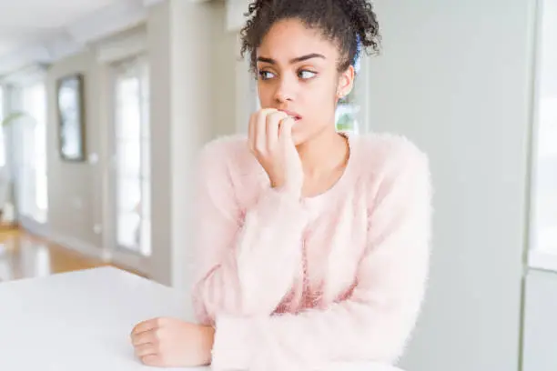 Photo of Beautiful young african american woman with afro hair looking stressed and nervous with hands on mouth biting nails. Anxiety problem.