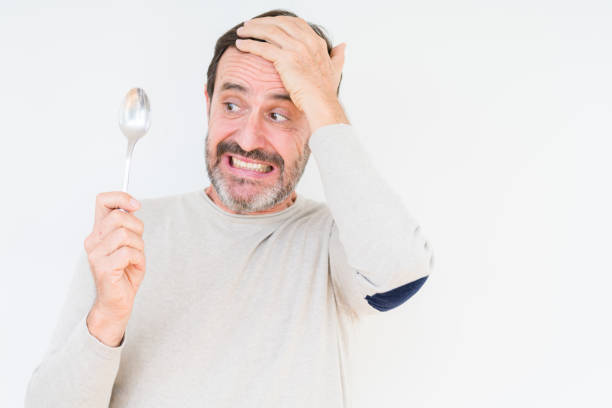 istock Senior man holding silver spoon over isolated background stressed with hand on head, shocked with shame and surprise face, angry and frustrated. Fear and upset for mistake. 1139078650