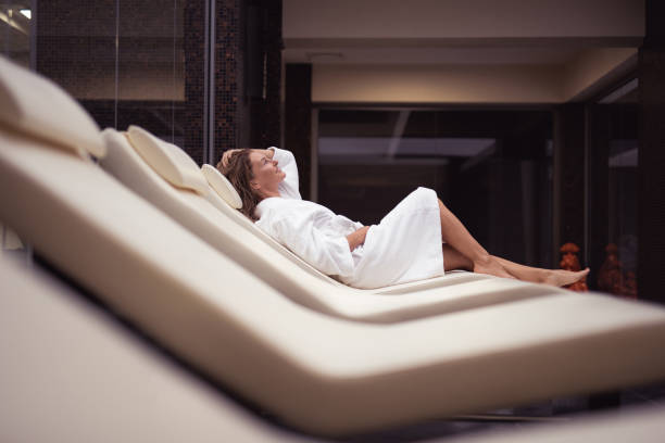 Gorgeous middle aged woman relaxing at luxury spa salon Perfect rest. Side view portrait of beautiful lady lying on daybed after shower. She is touching wet hair and looking up with smile chaise longue woman stock pictures, royalty-free photos & images
