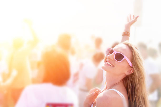 Woman loving the music concert, smiling and dancing with hand raised in the middle of the crowd.