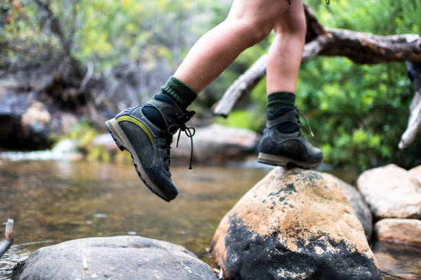 Woman wearing hiking boots jumps from rock to rock in a riverbed
