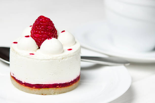 istock White airy cake with raspberry layer and raspberry berry lies on a white round plate next to a white cup, which stands on a white table 1139084228
