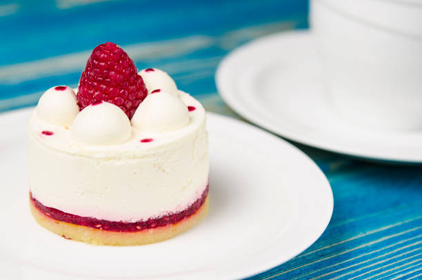 istock White airy cake with raspberry layer and raspberry berry lies on a white round plate next to a white cup, which stands on a blue table 1139084233