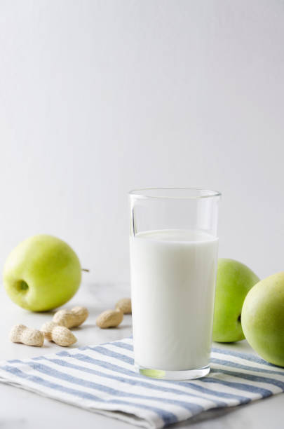 건강 한 아침 식사의 개념입니다. 화이트 테이블에 유백색 제품, 녹색 사과, 땅콩 및 냅킨의 유리. 세로 사진 - milky cheese 뉴스 사진 이미지