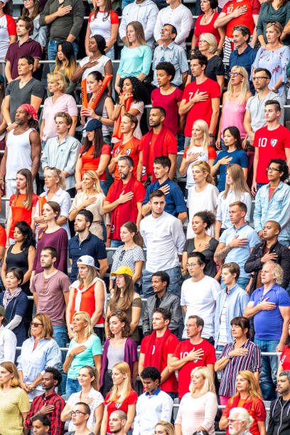 Standing crowd on a stadium during a national anthem with their hands on their hearts.