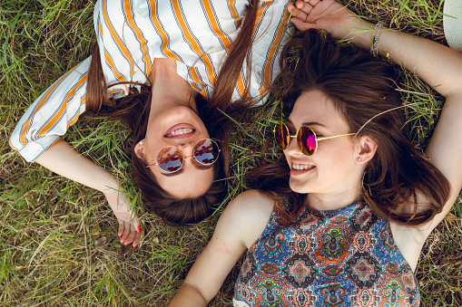 Two young women are lying down on grass in a park
