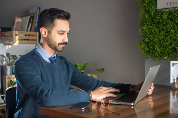 jeune homme d’asie du sud utilisant l’ordinateur portatif dans le bureau - technology typing male beauty asian and indian ethnicities photos et images de collection