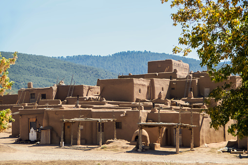 Multi-storied adobe mud Native American pueblo dwelling in the Southwestern United states with drying racks and outside ovens with mountains in the distance - selective focus
