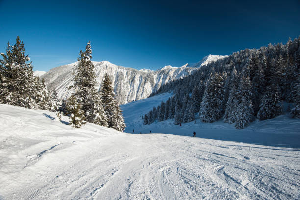 Panoramic landscape valley view with skiers going down a ski slope piste in winter alpine mountain resort