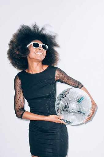 Smiling woman with sunglasses and black dress holding disco ball.