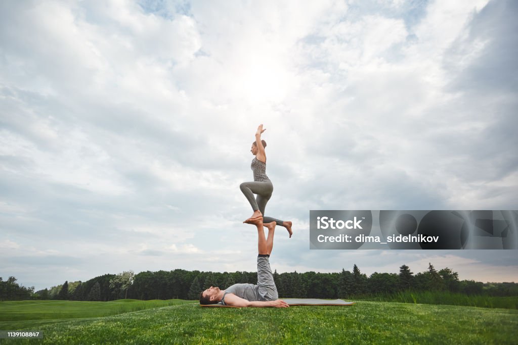 Ejercicios De Equilibrio Pareja Sana Y Joven Haciendo Yoga Acrobático En La Naturaleza Hombre Fuerte Acostado Sobre Una Alfombra Y Equilibrando A La Mujer En Sus Pies Foto de stock y más Ejercicios De Equilibrio Pareja Sana Y Joven Haciendo Yoga Acrobático En La Naturaleza Hombre Fuerte Acostado Sobre Una Alfombra Y Equilibrando A La Mujer En Sus Pies Foto de stock y más