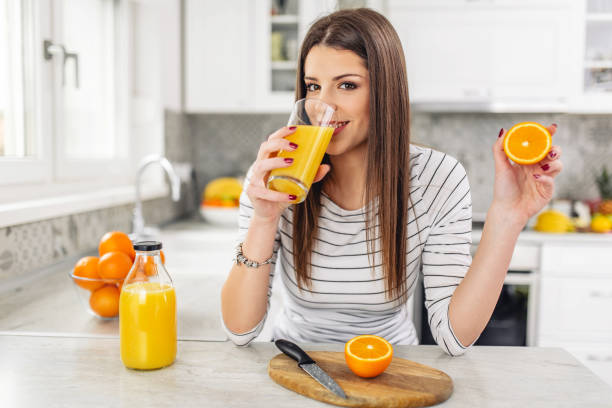 Close up Attractive Sensual Bare Woman drinking juice while Holding Sliced Orange Fruit. stock photo
