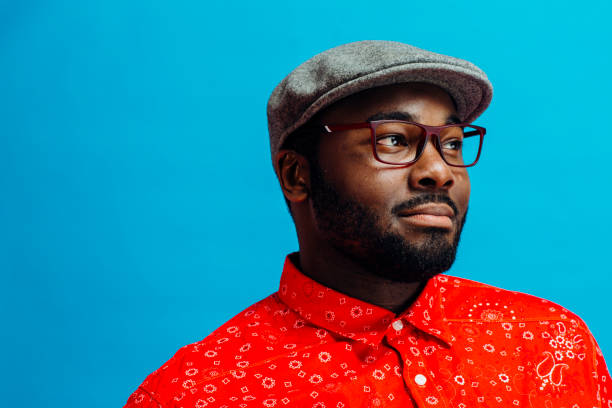 Man in bright red shirt, glasses and cap looking off camera Man in bright red shirt, glasses and cap looking off camera against bright blue background multi coloured glasses stock pictures, royalty-free photos & images