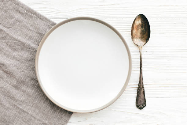 istock Stylish empty plate with vintage spoon on napkin on white table, flat lay. Modern set, serving for reception and celebration. Party and diet concept. Copy space 1139127290