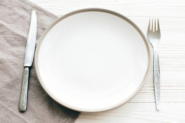 istock Stylish empty plate with vintage fork and knife on napkin on white table, top view. Modern set, serving for reception and celebration. Party and diet concept 1139127333