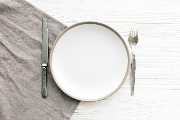 istock Stylish empty plate with vintage fork and knife on napkin on white table, flat lay. Modern set, serving for reception and celebration. Party and diet concept 1139127562