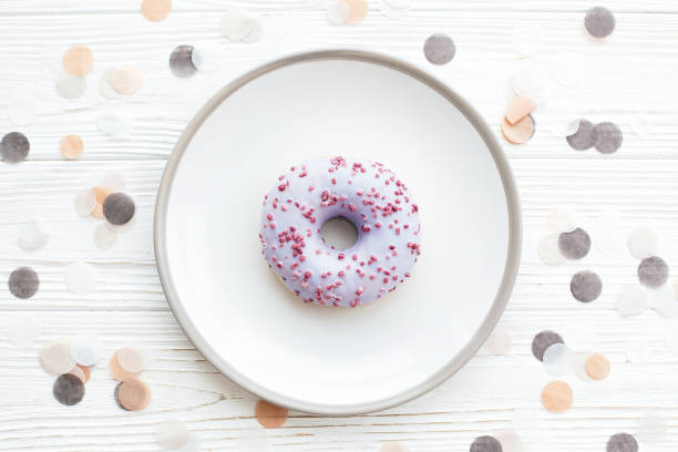 istock Delicious colorful donut with sprinkles on stylish plate on white table with confetti, flat lay. Party concept. No diet. Candy bar at wedding reception. Purple donut 1139127595