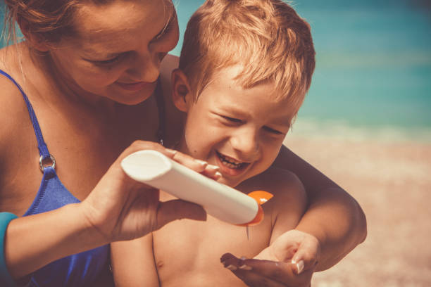 Mother applying sunscreen on son at the beach