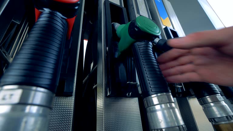 Close up of human hand putting out a green fuel nozzle. Gasoline fuel, gas station concept.